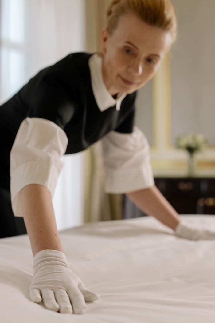 project-01-b A housekeeper elegantly arranges bed sheets in a luxurious hotel room, showcasing hospitality expertise.