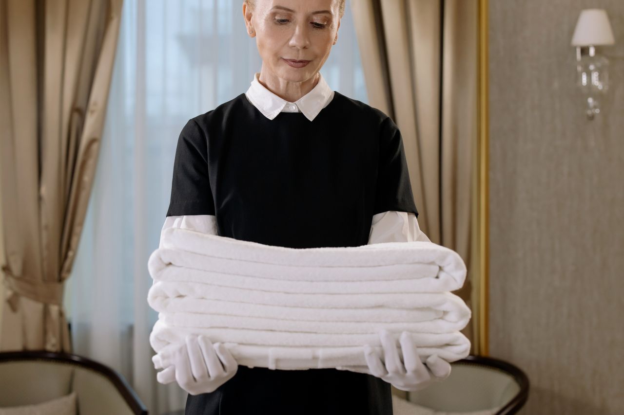 project-02-b Professional housekeeper holding a stack of fresh towels in a luxurious hotel room, showcasing elegance and service.